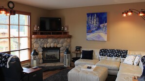 A cozy living room with a stone fireplace, a large flat-screen TV mounted above it, and a comfortable sofa set.