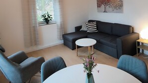 A modern living room with a round white table, grey sofas, a potted plant, and a painting on the wall. - Mountain apartment with Elbe and fortress view (Königstein)