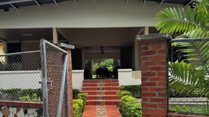 A covered outdoor area with a tiled walkway leading to a building entrance, surrounded by greenery and a brick wall. - 3-bedroom house in terrific Coronado Beach with WiFi, AC, BBQ area (Las Lajas)