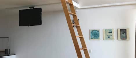 Una habitación con una escalera de madera, un televisor montado y obras de arte en la pared.