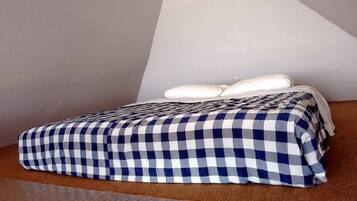 Una cama con colcha a cuadros y almohadas blancas en una habitación con techo inclinado y alfombra marrón.