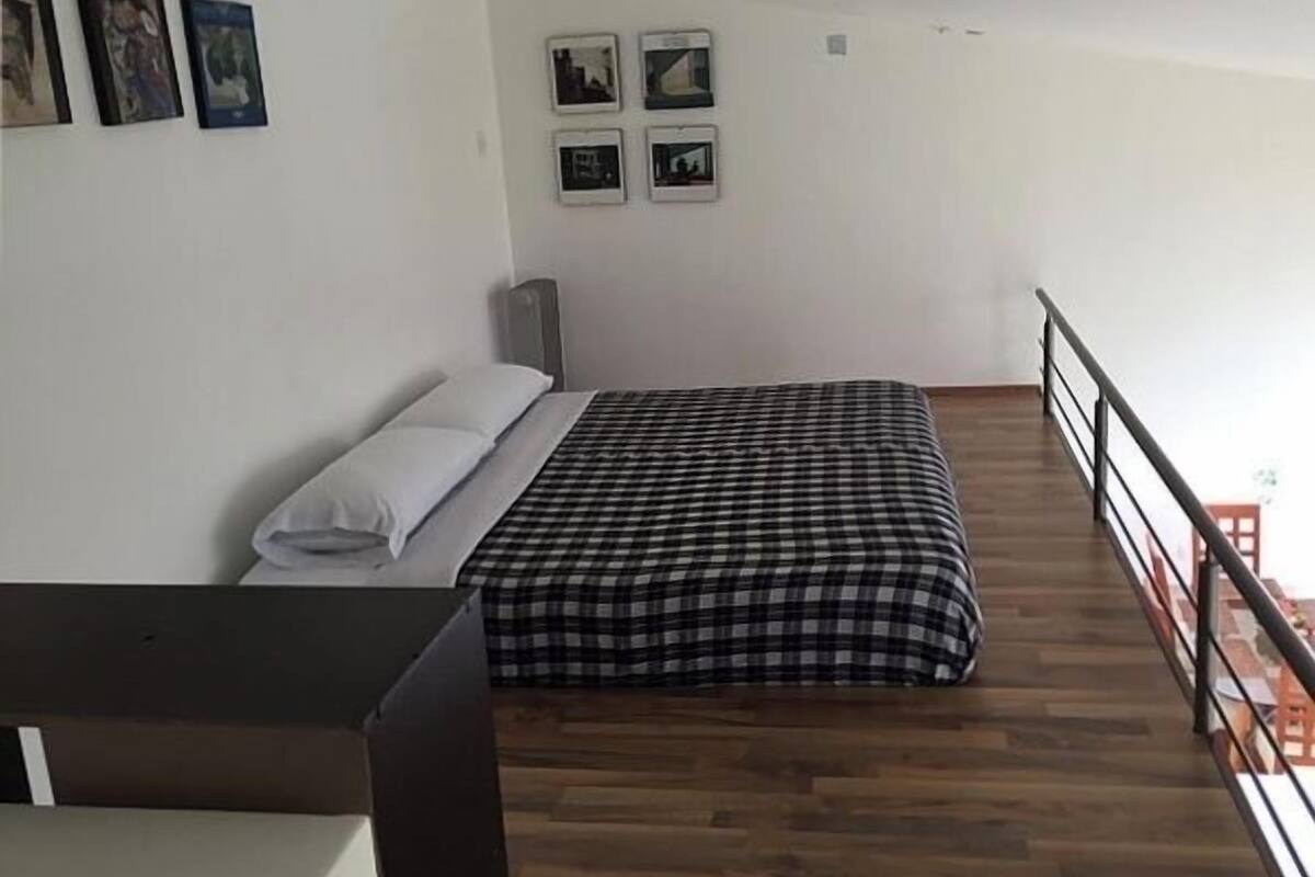 A bedroom with a bed, a desk, and a balcony with a railing.