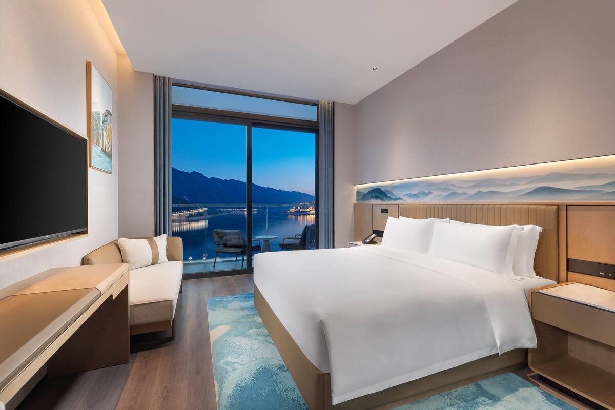 A modern hotel room with a large bed, a desk, a chair, and a TV.