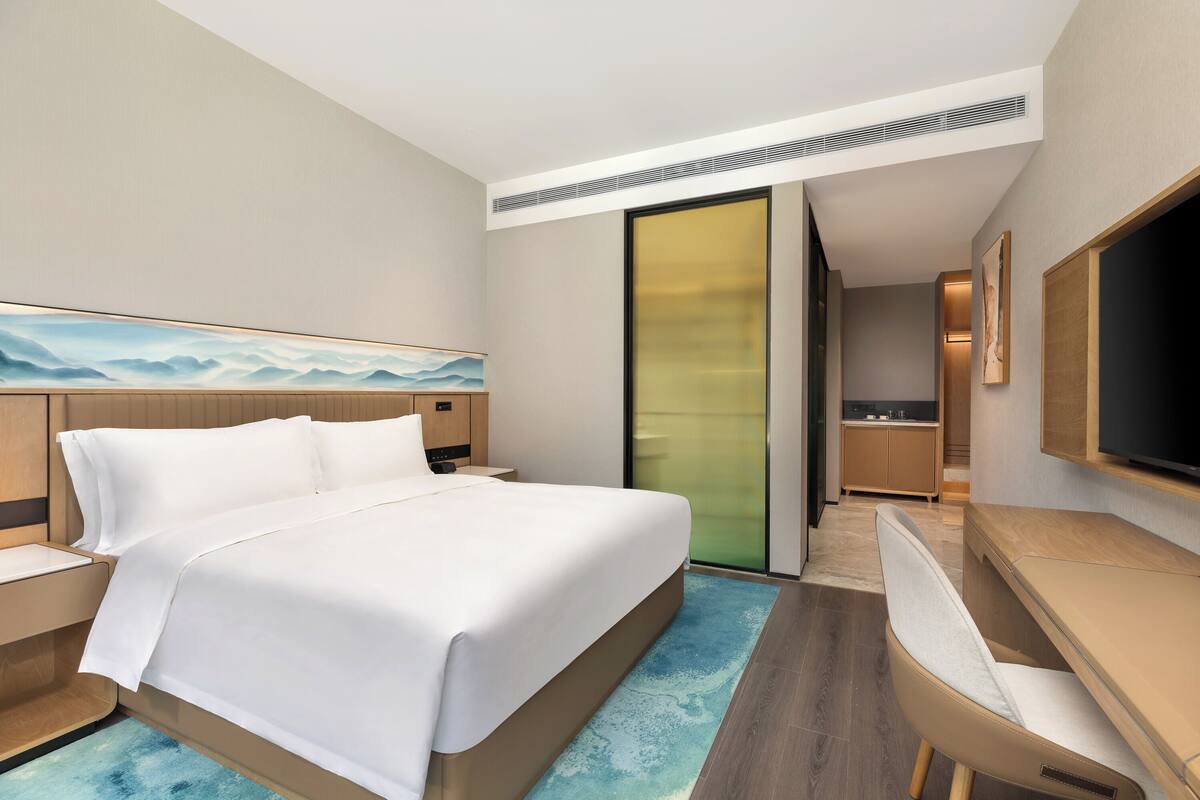 A modern hotel room with a large bed, a desk, and a television.