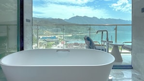 A modern bathroom with a freestanding bathtub, a glass-enclosed balcony with a view of a cityscape and mountains.