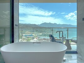 A modern bathroom with a freestanding bathtub, a glass-enclosed balcony with a view of a cityscape and mountains.