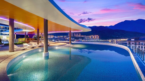 A modern infinity pool with a curved edge, surrounded by lounge chairs and a covered seating area.