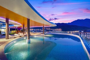 A modern infinity pool with a curved edge, surrounded by lounge chairs and a covered seating area.