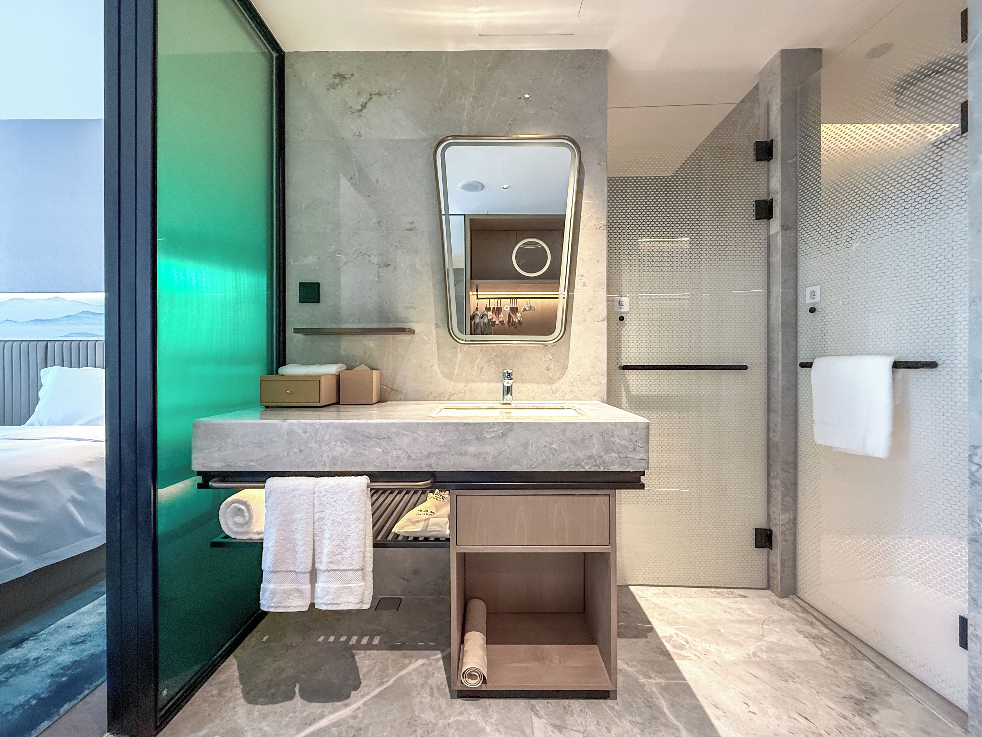 Un baño moderno con lavamanos de mármol, un espejo, toallero y zona de ducha.