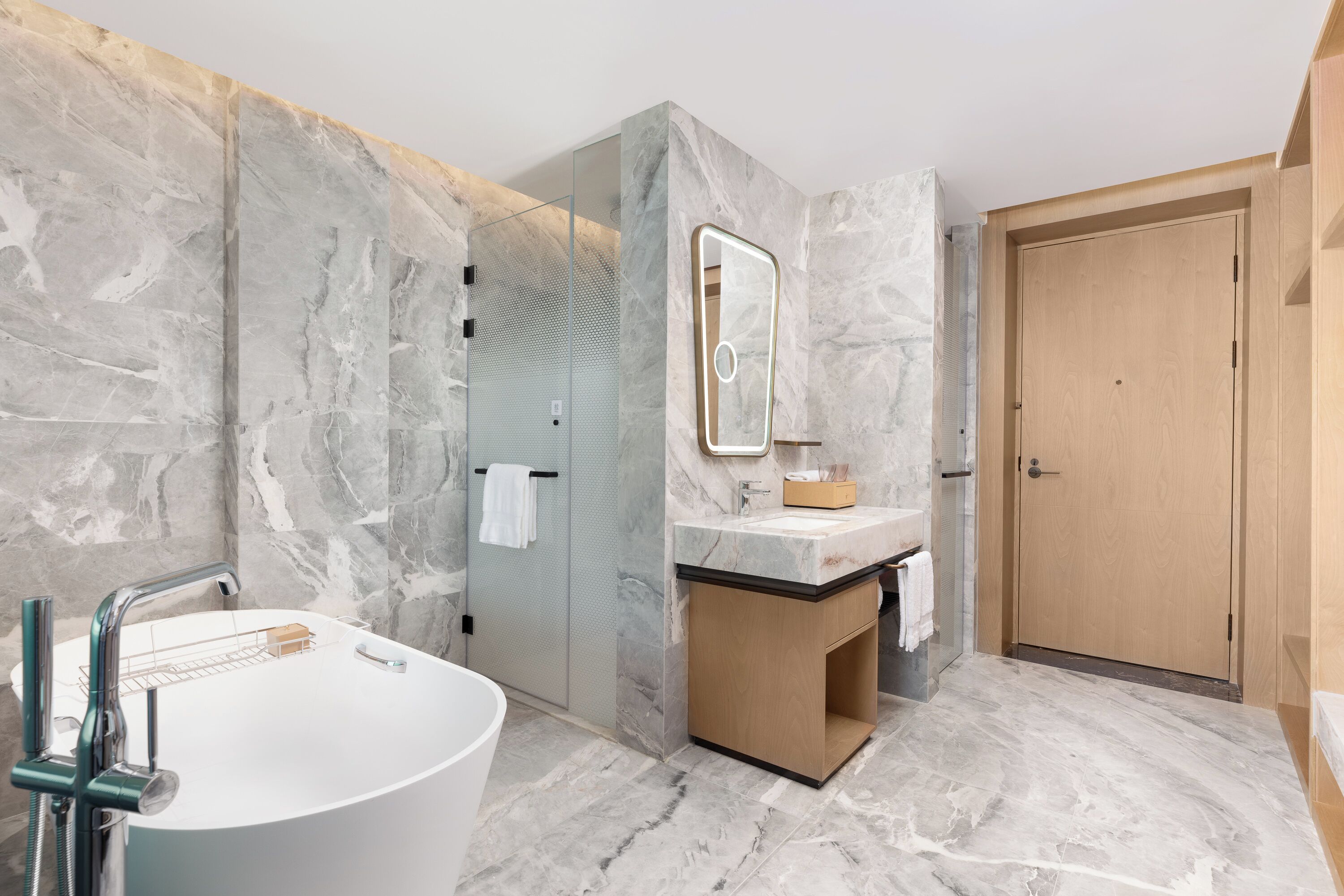 Un baño moderno con una bañera independiente, una ducha con cerramiento de vidrio y un mueble de tocador de madera.