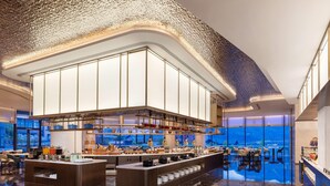 A modern hotel lobby with a central bar area, seating arrangements, and a view of the cityscape through large windows.