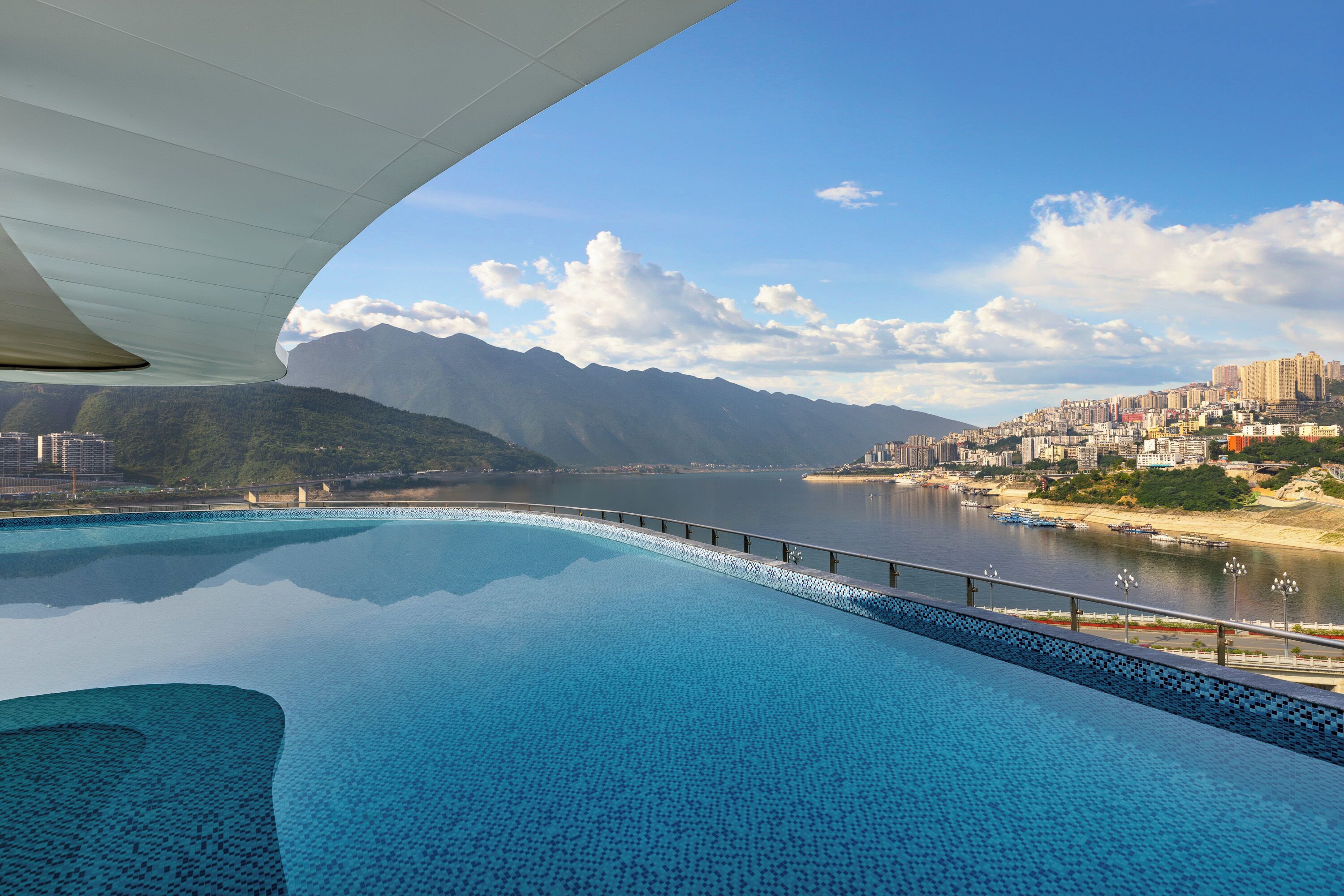 A large, clear swimming pool with a view of a cityscape and mountains in the background.