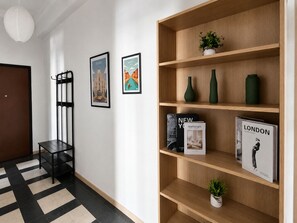 Ein Korridor mit einem schwarz-weißen Schachfußboden, einem Holzregal mit Büchern und Dekorationsobjekten sowie zwei gerahmten Bildern an der Wand.