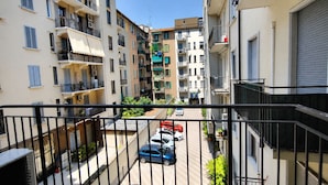 A residential building with multiple balconies, a narrow street, and parked cars.