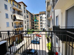 Ein Wohngebäude mit mehreren Balkonen, eine schmale Straße und geparkte Autos.