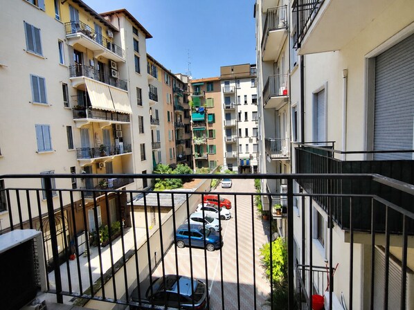 Un edificio residencial con varios balcones, una calle estrecha y coches aparcados.
