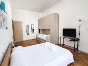 Una habitación de hotel con una cama, un televisor sobre un mueble bajo, un armario y una puerta.