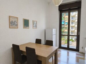 Ein Essbereich mit Tisch und Stühlen, einem Kühlschrank und Blick auf ein Wohngebäude durch eine Glastür.