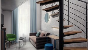 A modern living room with a staircase, a green chair, a sofa, and a small table. - EA Hotel Moment Self Check-In (Prague)