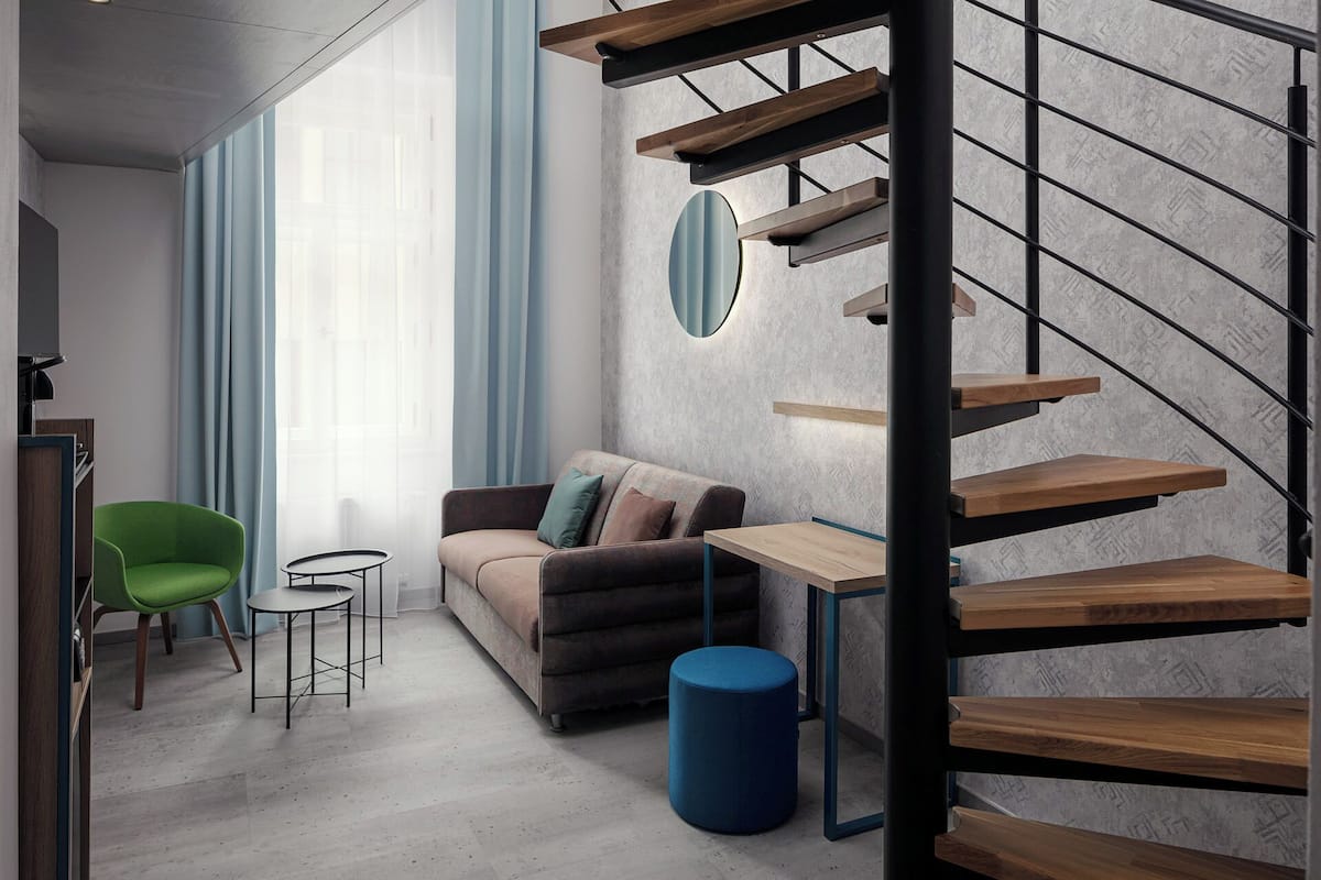 Un salon moderne avec un escalier, un fauteuil vert, un canapé et une petite table.
