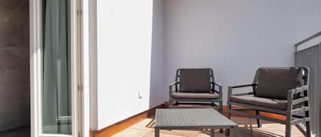 An outdoor balcony with two chairs and a table, a sliding glass door, and a red fire alarm.
