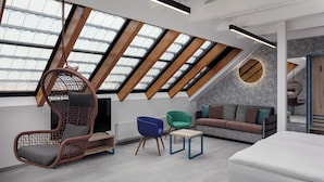 A modern loft bedroom with a sloped ceiling, skylights, a hanging chair, a sofa, and a bed. - EA Hotel Moment Self Check-In (Prague)
