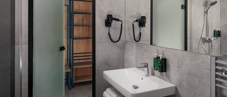A modern bathroom with a white sink, a mirror, and a shower. There is a towel rack and a wooden shelf.