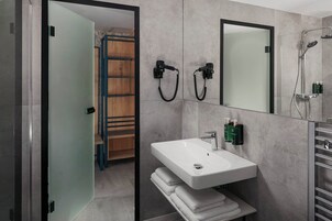 Un bagno moderno con un lavandino bianco, uno specchio e una doccia. È presente un portasciuga e una mensola in legno.