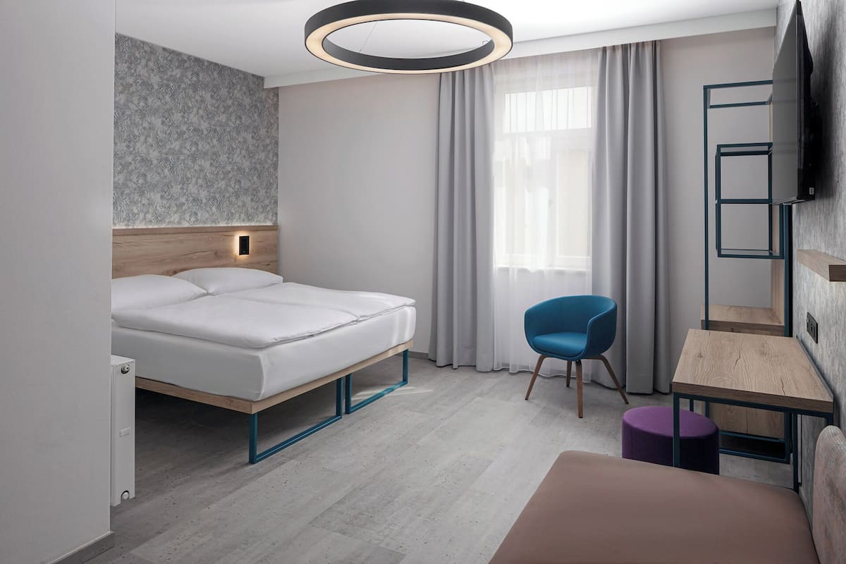 Une chambre d’hôtel moderne équipée d’un lit, d’un bureau, d’une chaise et d’un téléviseur fixé au mur.