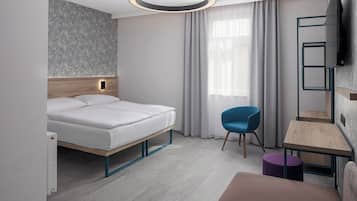 Ein modernes Hotelzimmer mit einem Bett, einem Schreibtisch, einem Stuhl und einem an der Wand befestigten Fernseher.