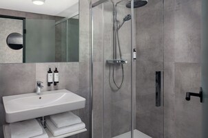 Un bagno moderno con doccia vetro, lavandino bianco e due flaconi di shampoo.