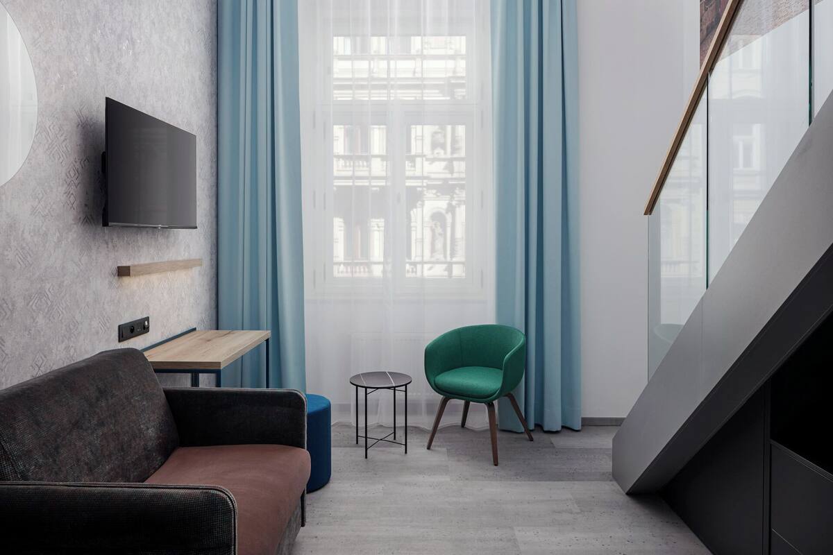 Un salon moderne avec un canapé, une petite table, un fauteuil vert et un téléviseur fixé au mur.