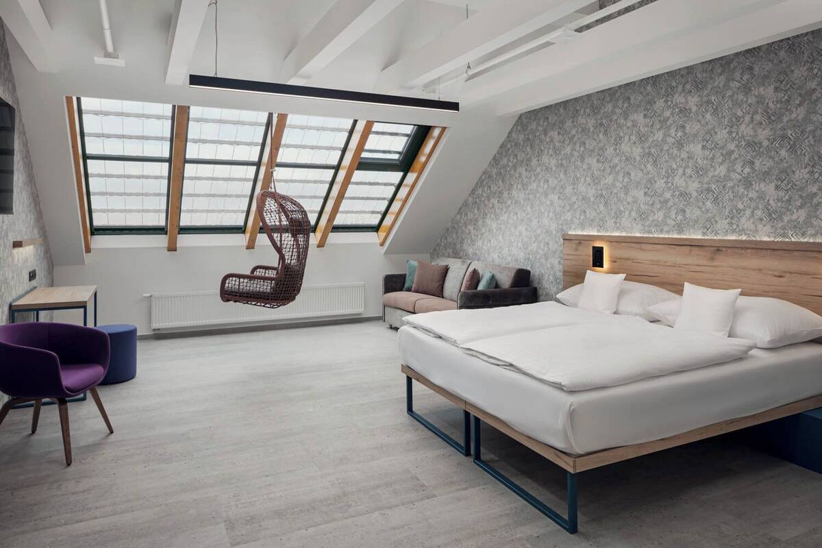 Une chambre moderne avec un grand lit, un fauteuil suspendu, un canapé et un bureau.