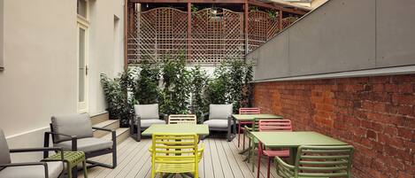 An outdoor patio with multiple tables and chairs, a wooden deck, and a brick wall.