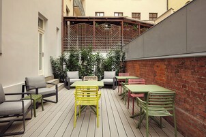 Um pátio externo com várias mesas e cadeiras, um deck de madeira e um muro de tijolos.