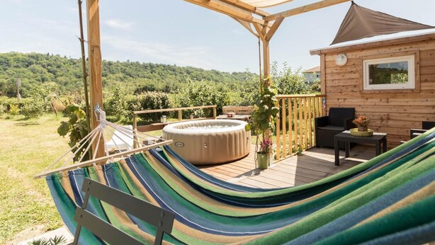 Una terraza de madera con una hamaca, un jacuzzi y una cabaña de madera con ventana.
