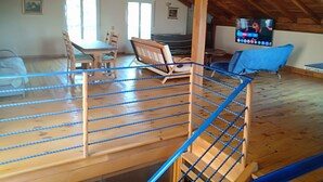 An attic room with a wooden floor, a blue chair, a dining table with chairs, and a television.