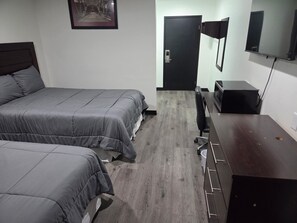 A hotel room with two beds, a desk, a chair, a TV, and a door. - The Suite Inn (Minot)