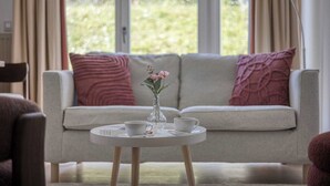 Ein Wohnzimmer mit einer Couch, zwei Kissen, einem kleinen Tisch mit Blumenvase, einer Tasse und einem Teekessel.