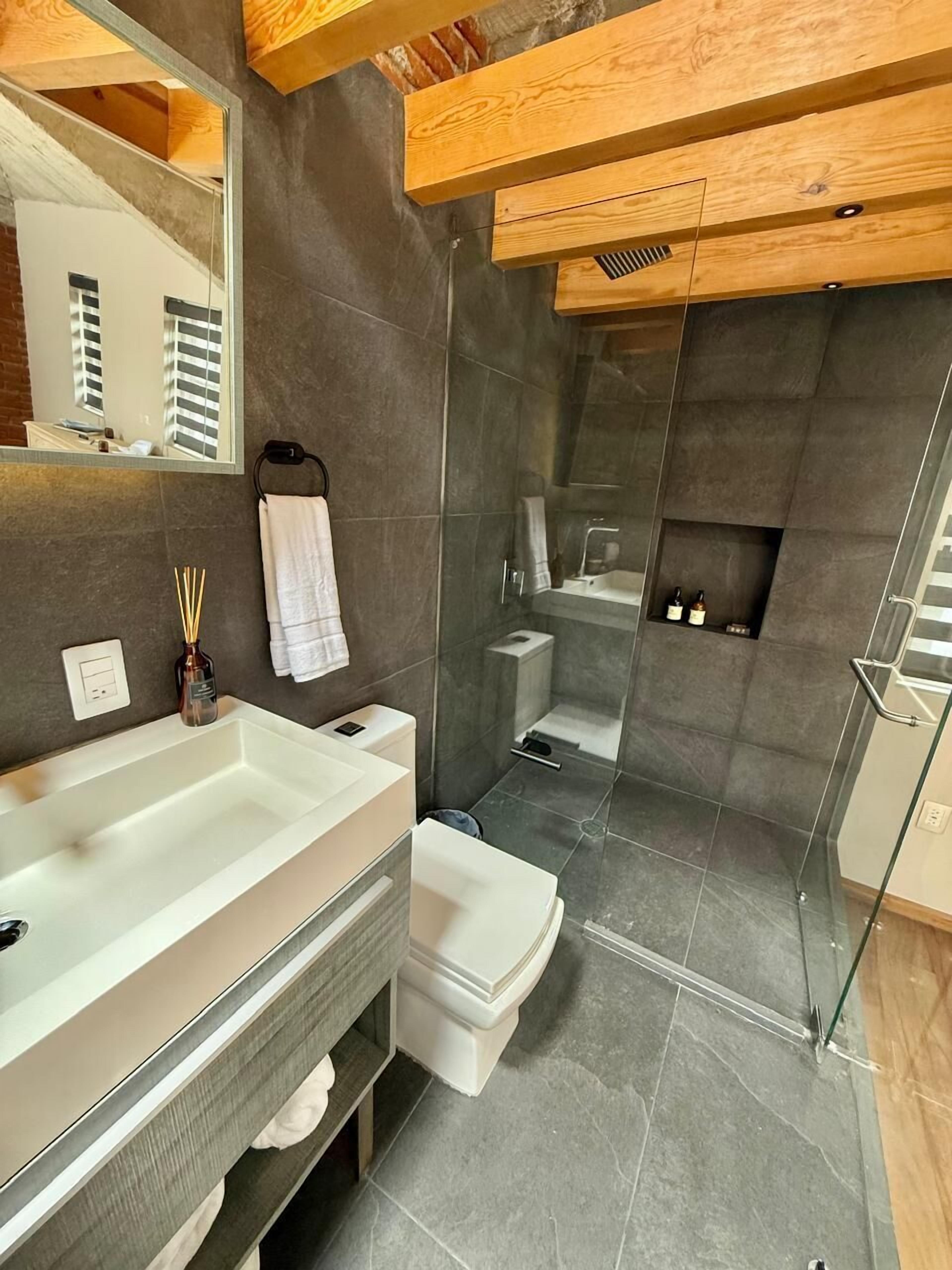 Un baño moderno con un espejo grande, un lavabo blanco, un inodoro y una zona de ducha.