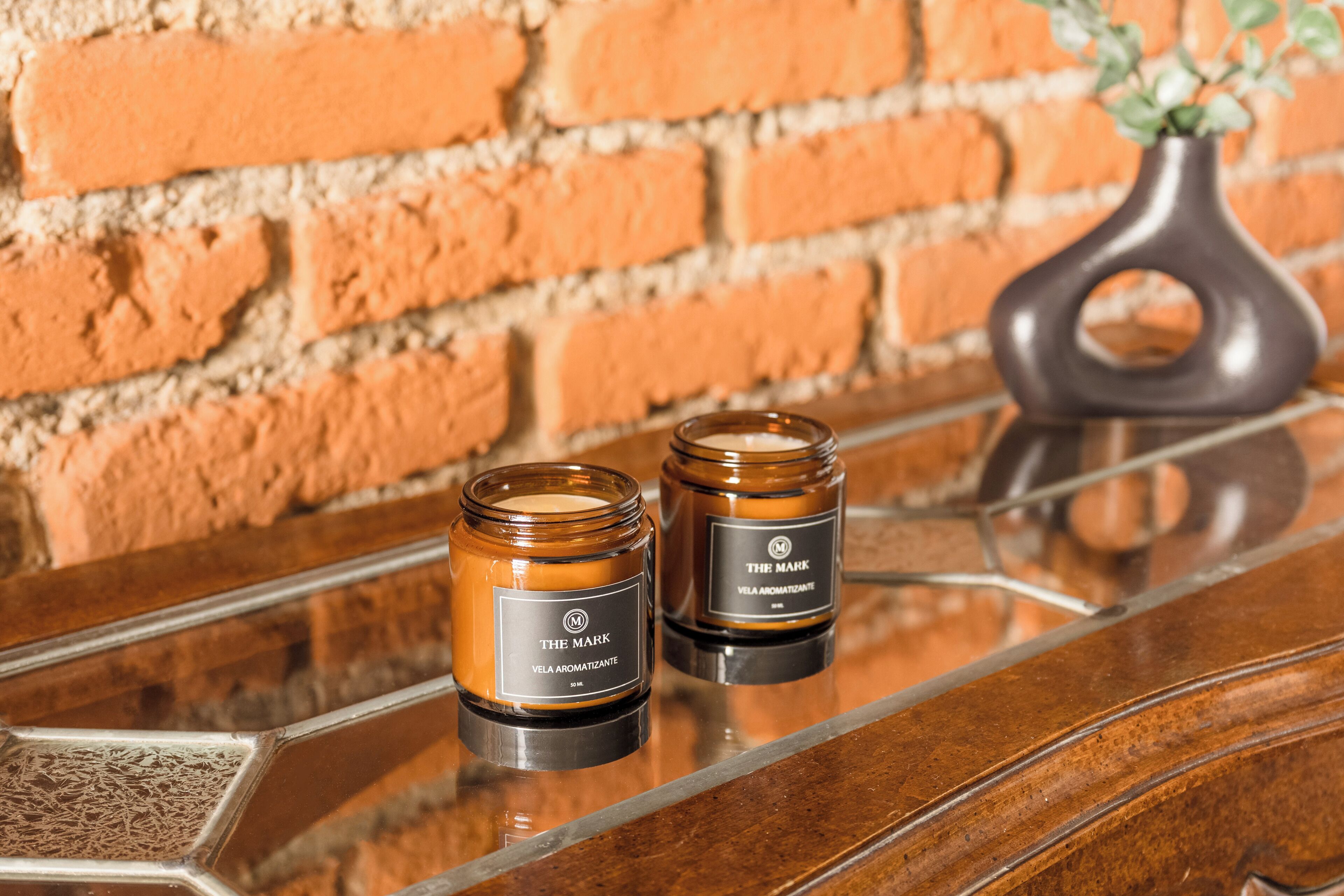 Two amber-colored candles on a reflective surface with a brick wall in the background.