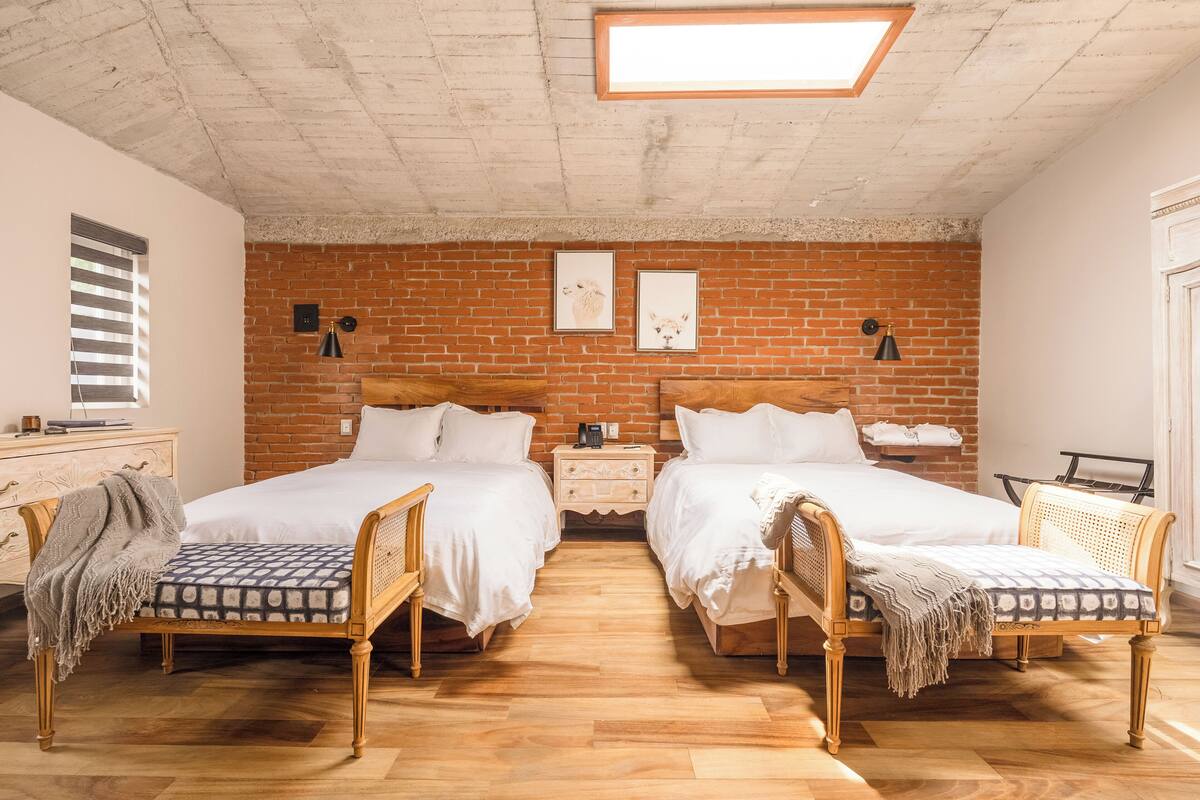 Une chambre avec deux lits, un mur en briques, un plancher en bois et une lucarne.