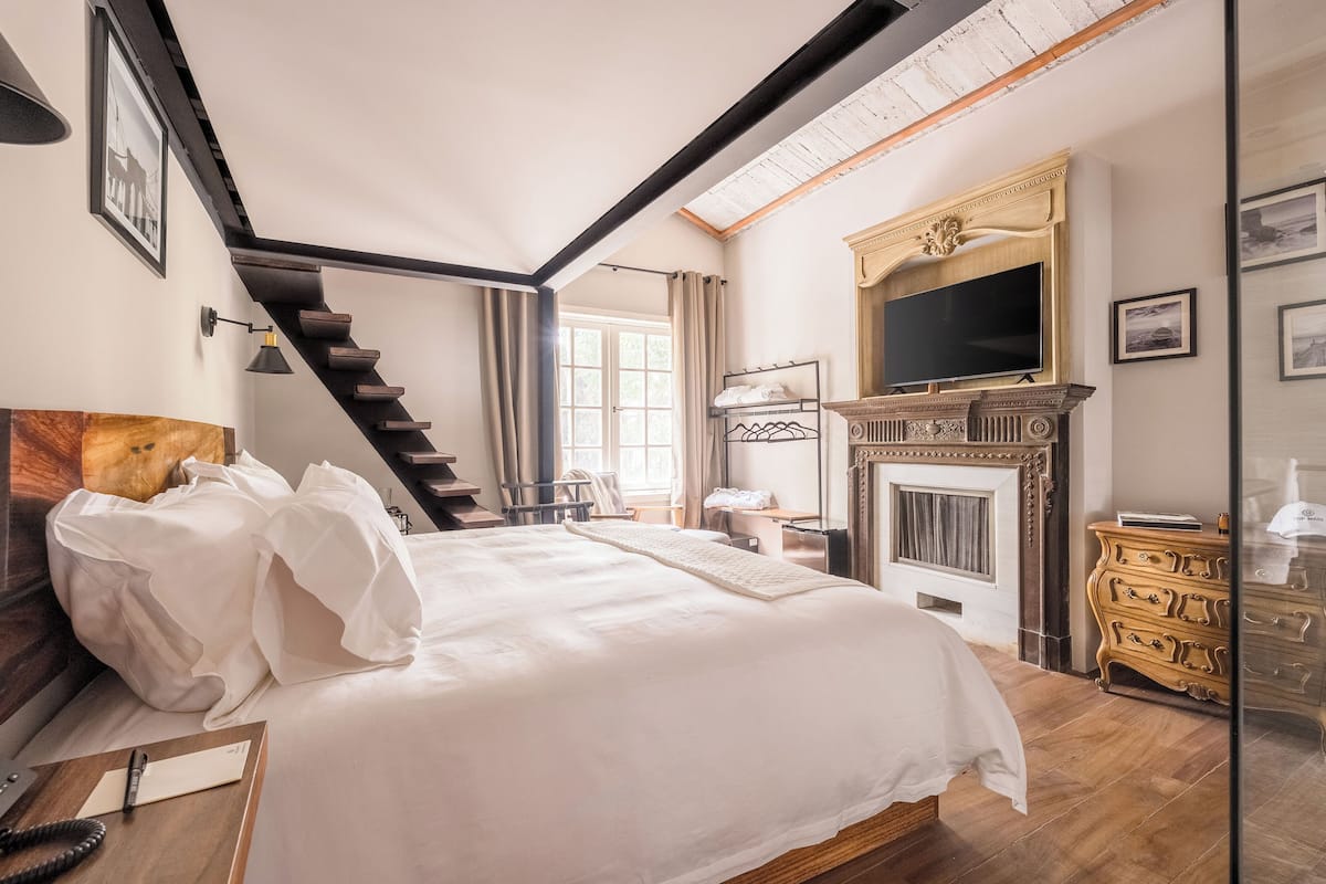 Une chambre à coucher avec un grand lit, une commode en bois, une cheminée, un téléviseur et un escalier.