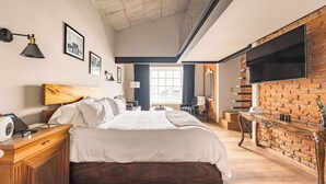 Un dormitorio moderno con una cama grande, cabecera de madera, televisor de pantalla plana montado en una pared de ladrillo y un escritorio con lámpara.
