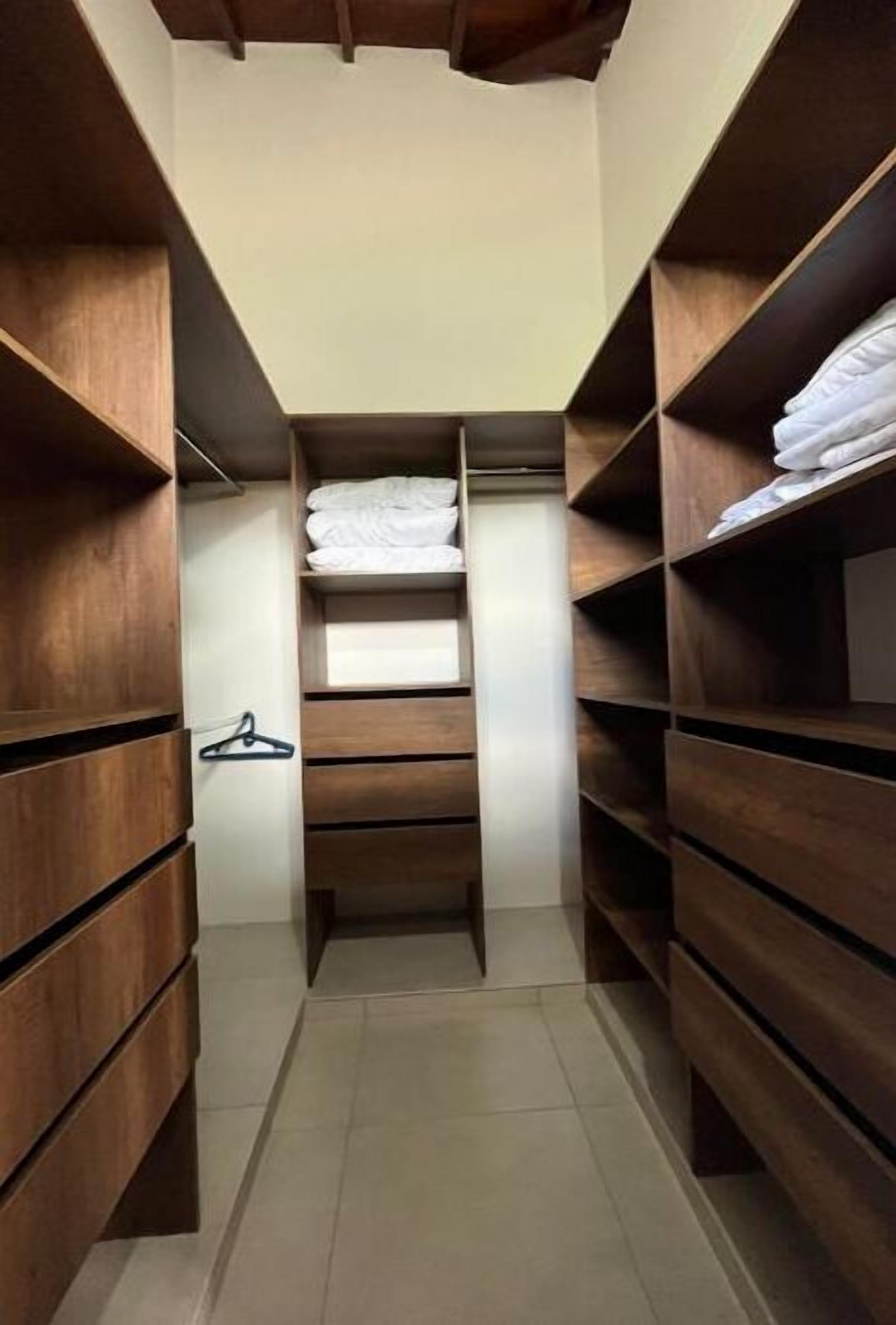 A narrow walk-through closet with wooden shelves and a hanging rack.
