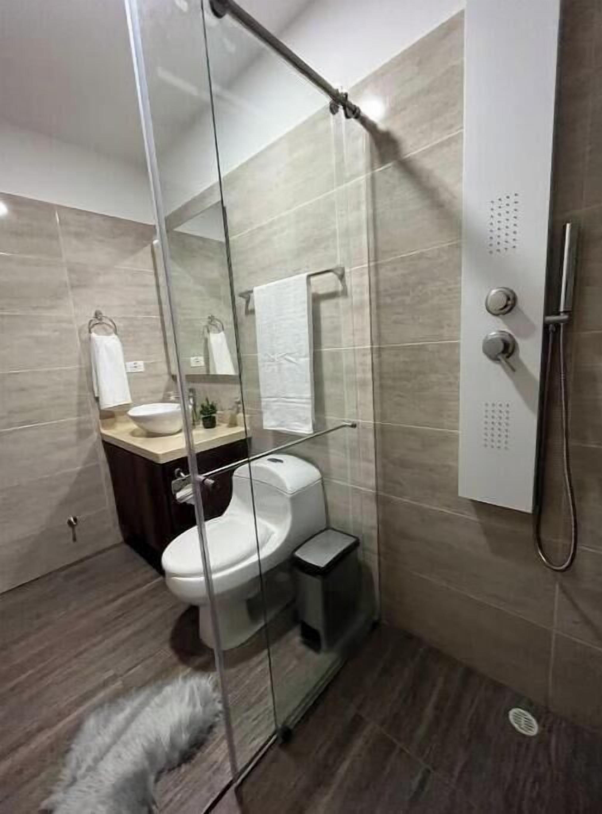 Un bagno moderno con doccia vetro, WC e lavandino con specchio sopra.