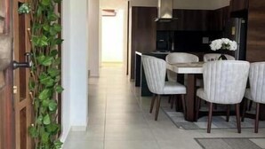 Une cuisine moderne avec des meubles de couleur bois foncé, un plan de travail blanc et un coin repas comprenant quatre chaises et une table.