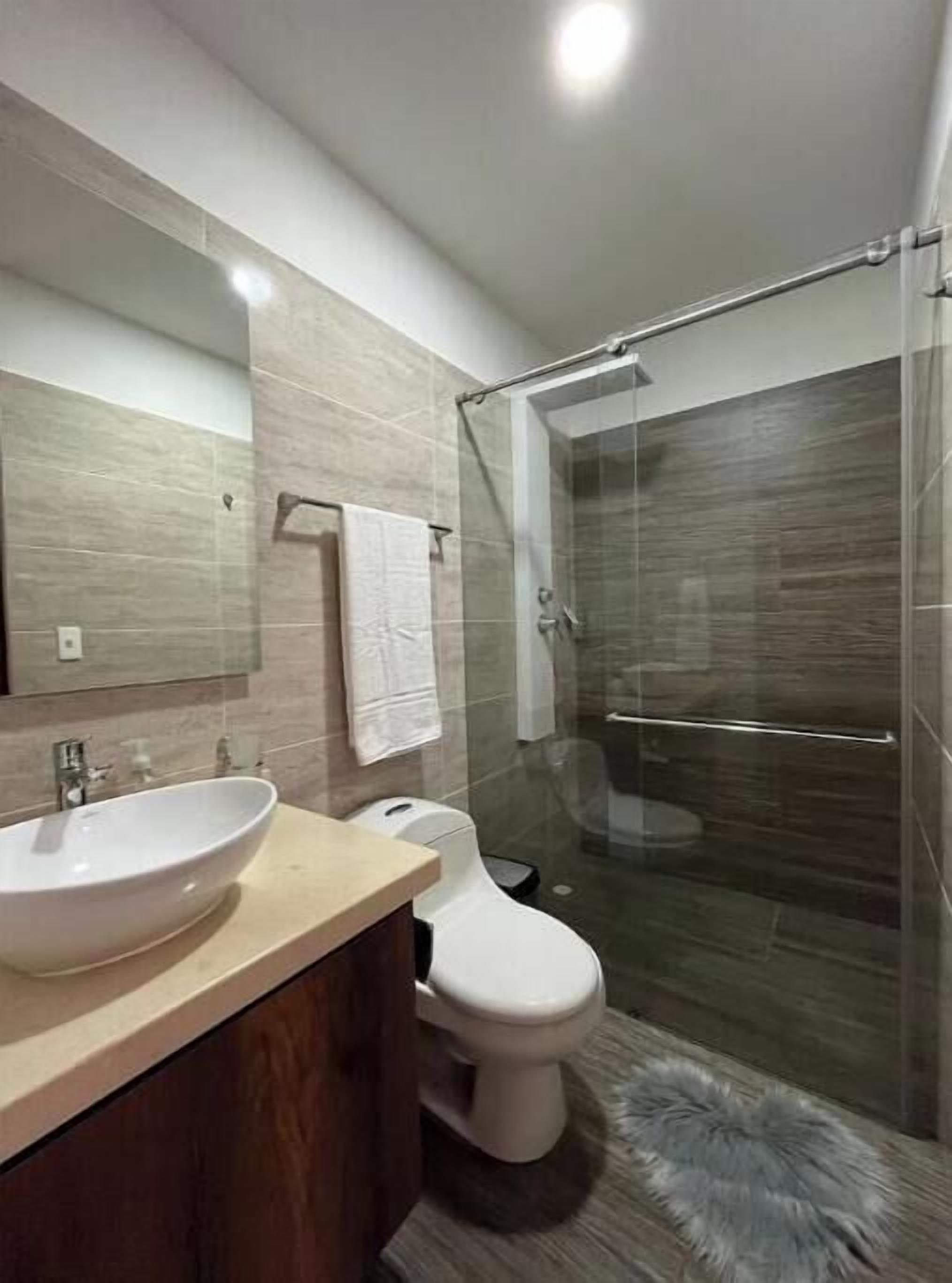 A modern bathroom with a large mirror, a sink, a toilet, and a glass-enclosed shower.