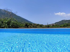 A clear blue pool with a tiled bottom, surrounded by lush greenery and hills in the background.