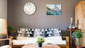 A cozy living room with a wooden sofa, a round wall clock, a framed painting, and a wooden cabinet. - Maison la Gileppe (Jalhay)
